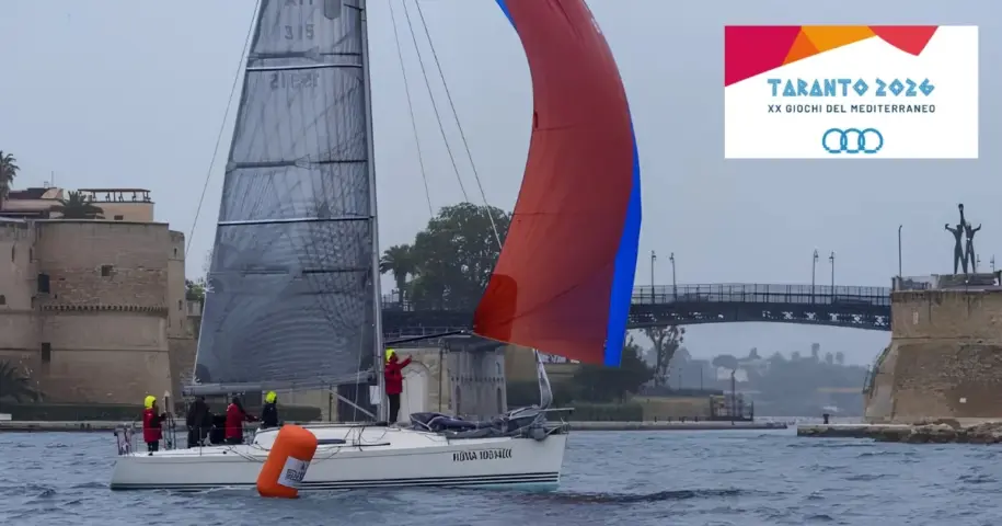 Barca a vela nel canale navigabile di Taranto con logo ufficiale dei Giochi del Mediterraneo 2026