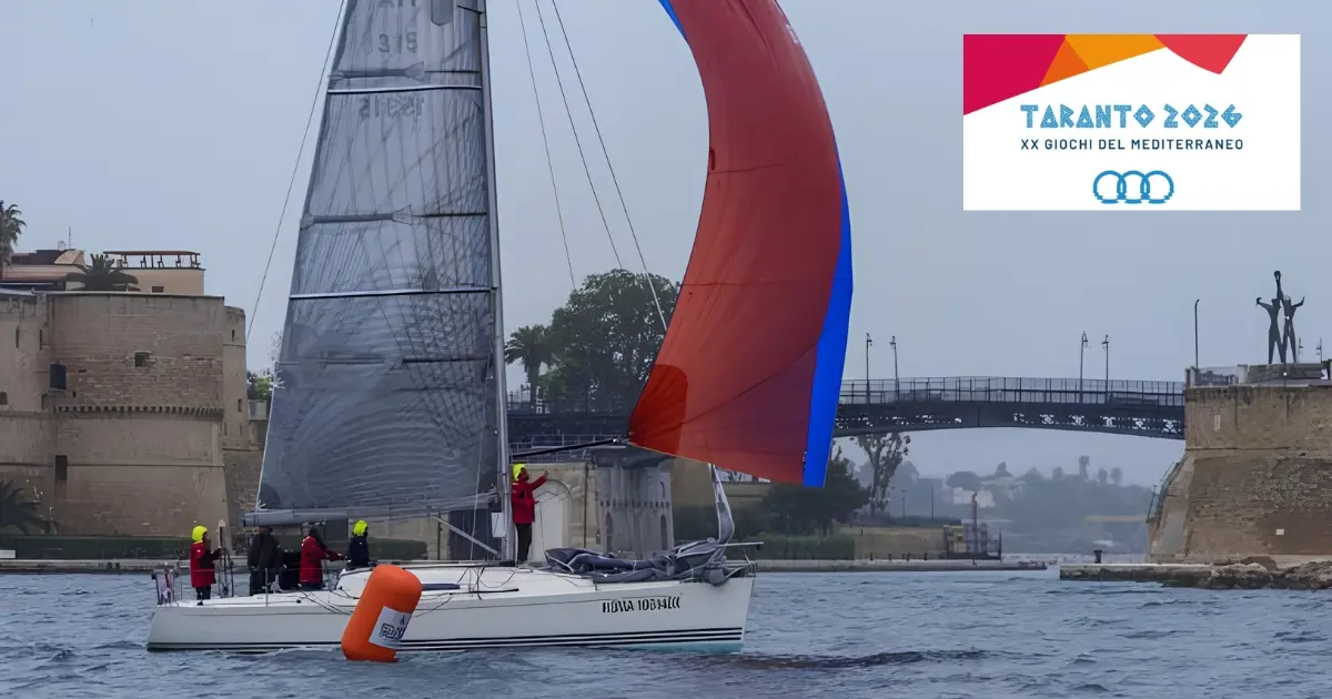 Barca a vela nel canale navigabile di Taranto con logo ufficiale dei Giochi del Mediterraneo 2026
